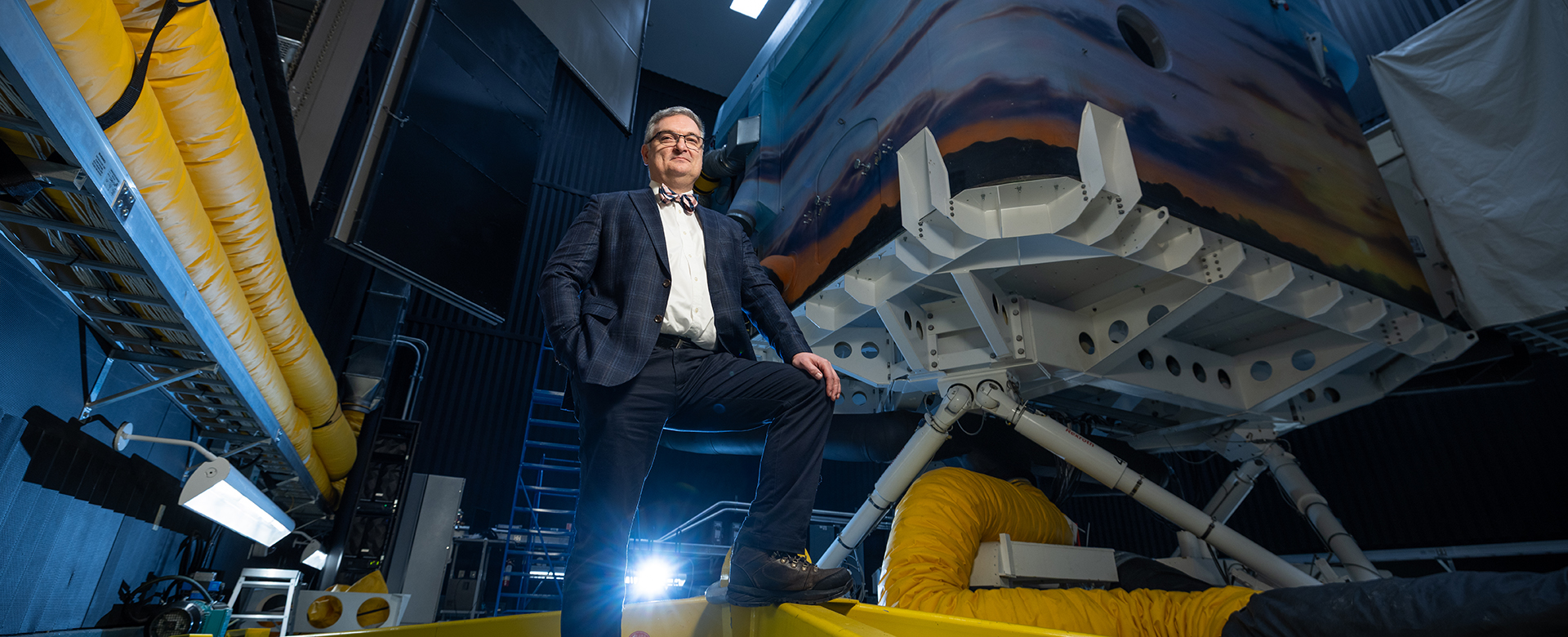 The CEO of KITE Research Institute stands in a suit and bow tie in front of a futuristic research lab