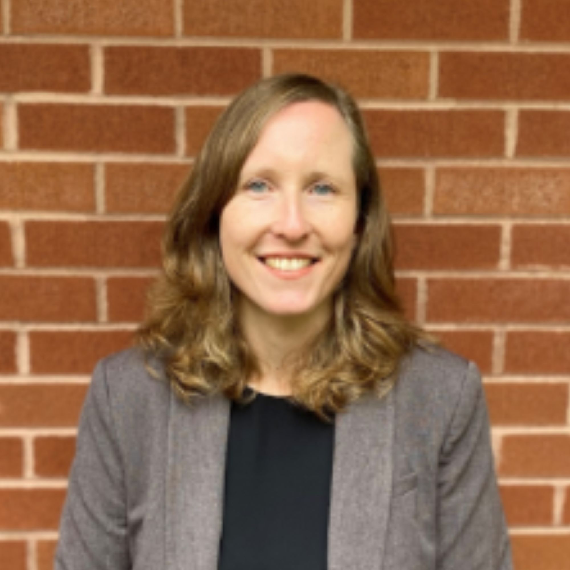 A headshot of a woman standing in front of a brick wall