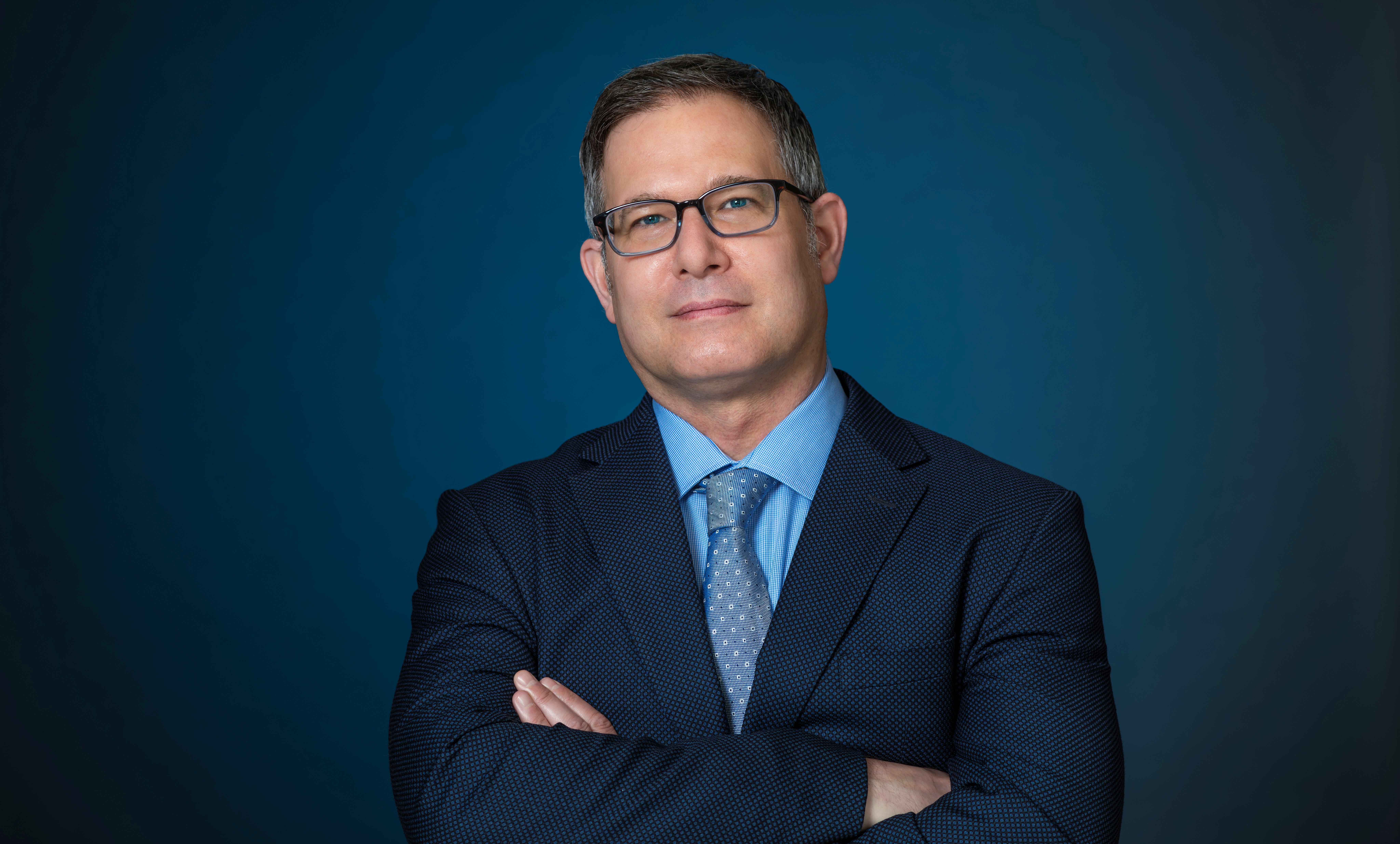 Headshot of a man wearing eye glasses and a suit and tie
