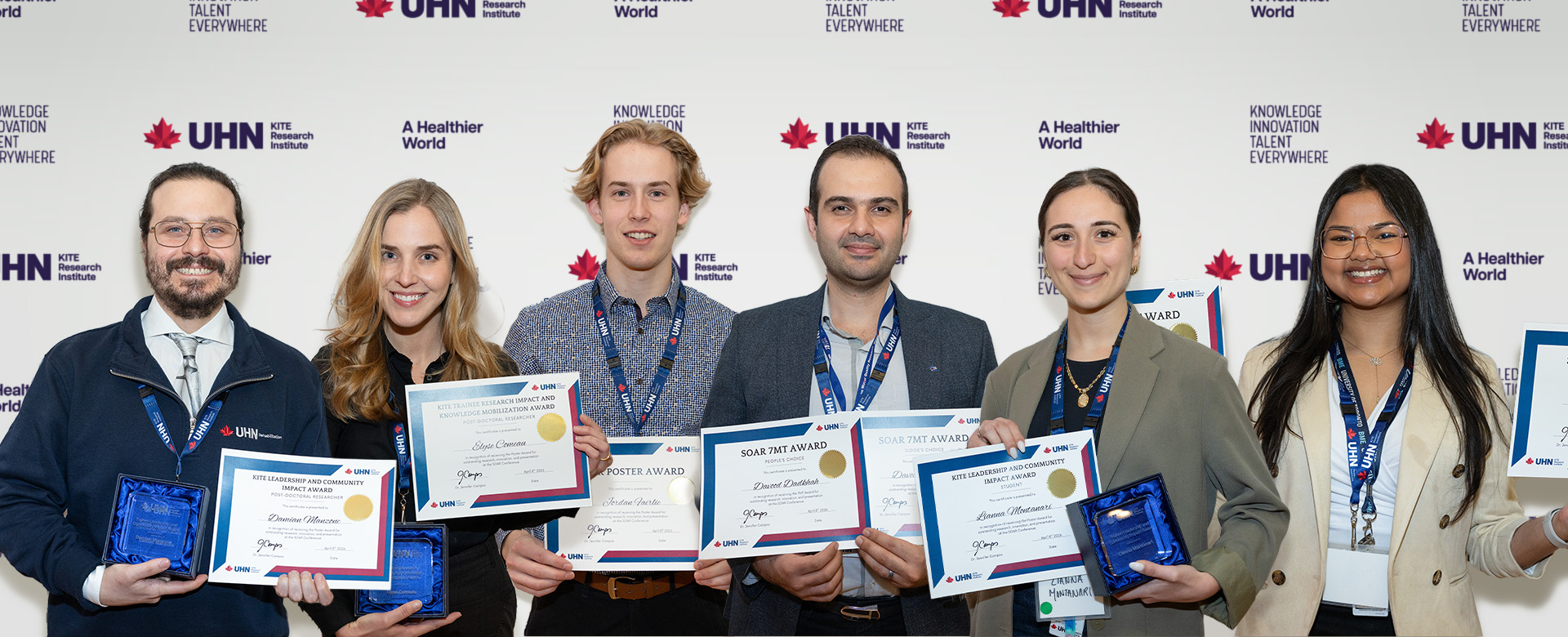 Six trainees pose with their paper awards in front of a KITE UHN banner. 