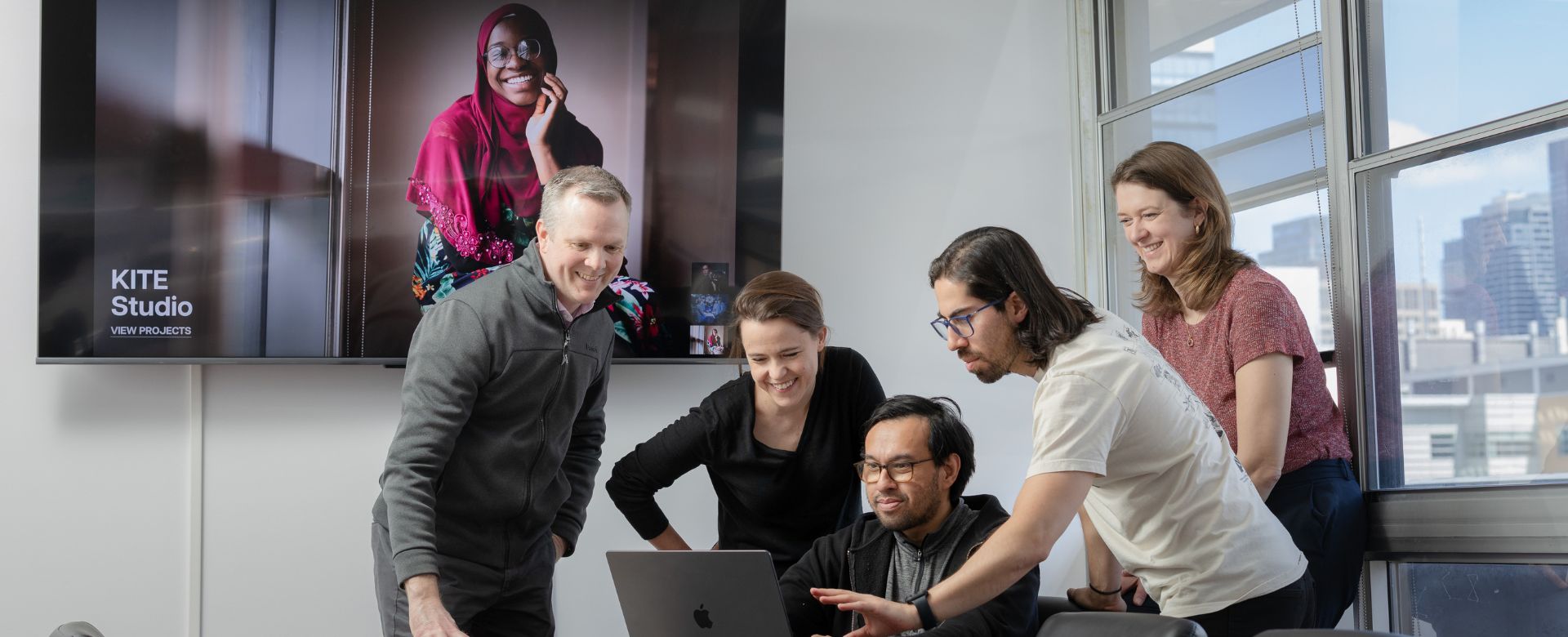 Five people gathered around a computer screen in a modern board room 