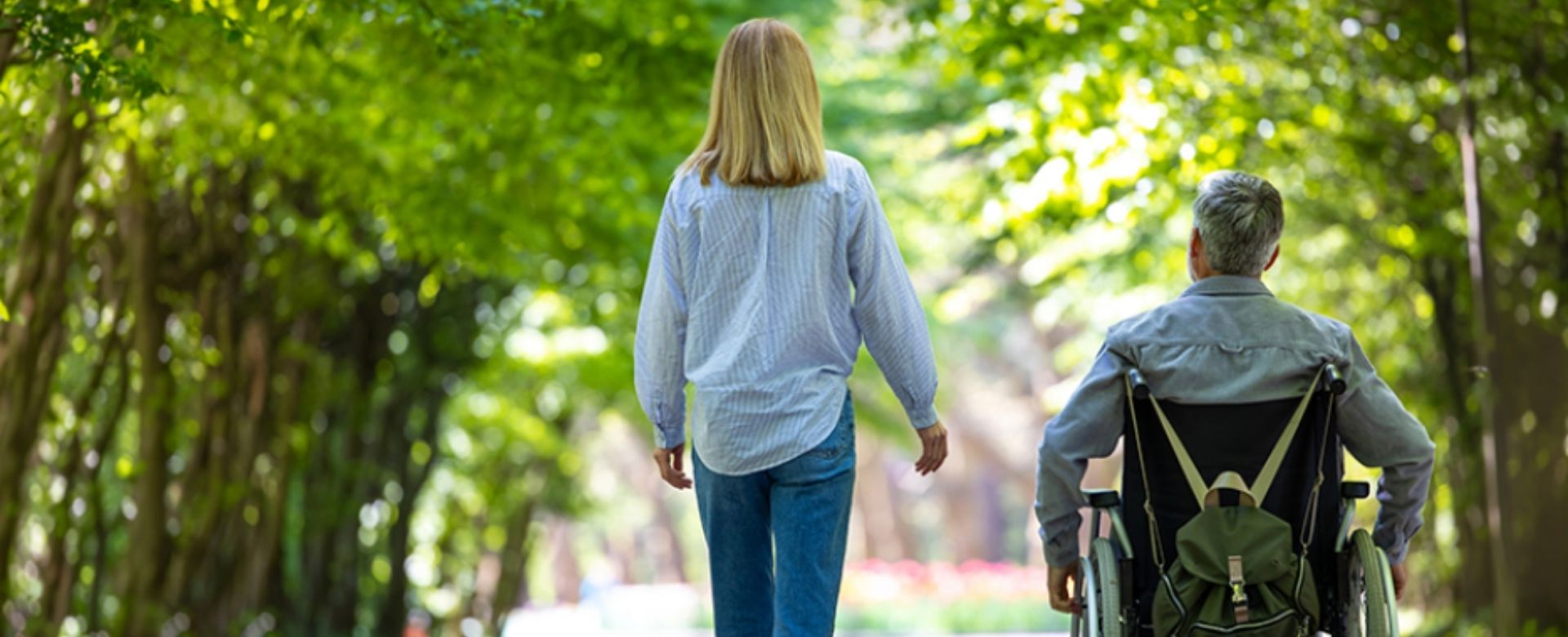 A woman walks next to a man in a wheelchair down a path. 