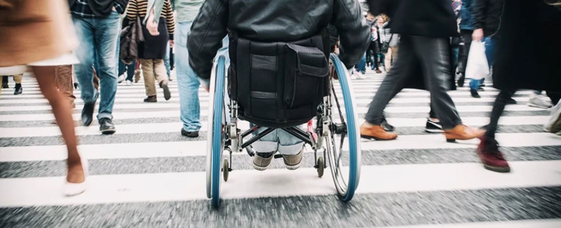 A man in a wheelchair crosses a busy street at an intersection