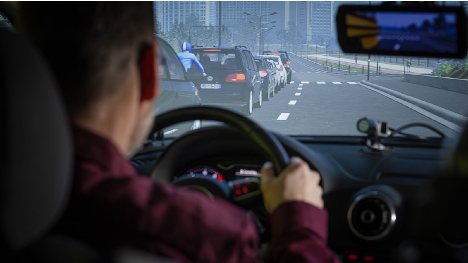 Over the shoulder shot of a man driving in DriverLab, where he engages in a simulation where he's driving down a city street.